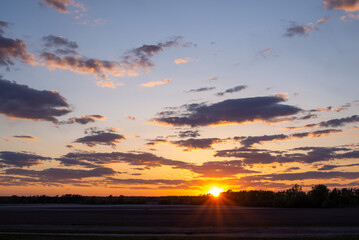 Bright sunlight on horizon, last rays of the sun above the agricultural field. Beautiful sunset,...