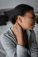 Side view of multiracial woman suffering from neck pain on bed at home.