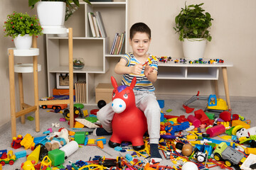 A little boy is jumping on an inflatable rubber donkey among the mess in the children's room....