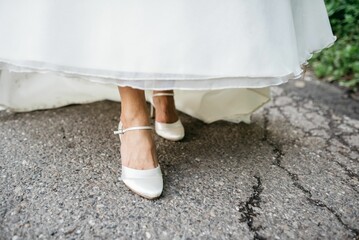 Bride wearing a white gown with a sheer skirt, standing outdoors in a sunny environment