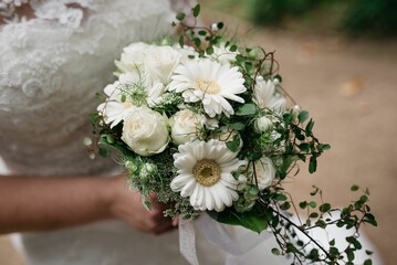 Image of a white bridal bouquet filled with lush flowers in the hands of a bride in a white dress