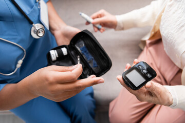 top view of multiracial nurse in uniform holding test strip near senior woman holding lancet pen and glucometer.