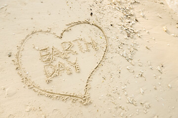 The word EARTH DAY is writting on the sand inside heart shaped sand writing. drawing on the sand. writing with sands on the beach.