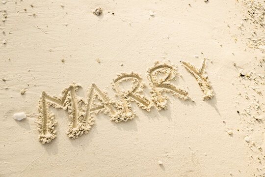 The word MARRY is writting on the sand. drawing on the sand. writing with sands on the beach.