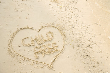 The word CHILD FREE is writting on the sand inside heart shaped sand writing. drawing on the sand. writing with sands on the beach.