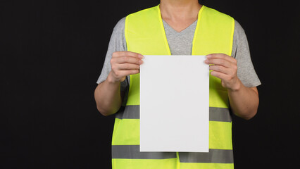 Blank empty paper in man hand and wear safety Vest on black background.