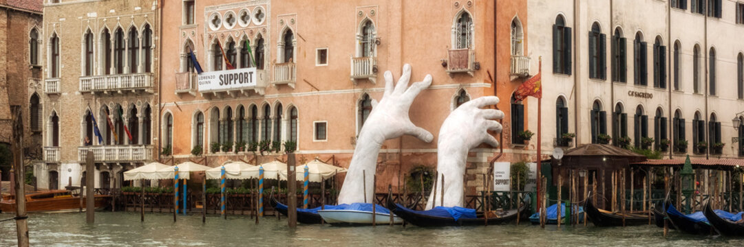 ENICE, ITALY - SEPTEMBER 12, 2017:  Panorama view of sculpture titled "Support" by artist Lorenzo Quinn  for the 2017 Venice Biennale.  The Giant hands support the sides of the Ca’ Sagredo Hotel 