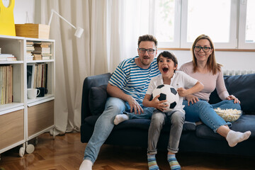 Family of 3 is sitting on the sofa and watching a football game