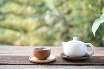 white tea cup and tea pot and on wooden tray and table balcony outdoor view with green background