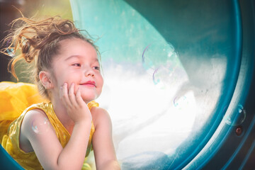 beautiful junior little girl playing in the park in yellow dress laughing with bubbles, screaming...