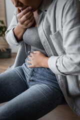 Cropped view of blurred multiracial woman suffering from stomach ache at home.