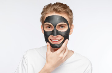 Beautician doing carbon peeling procedure to handsome guy in beauty salon. Black clay mask on the face of a young man. Hardware male cosmetology.