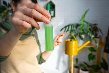 Drip fertilizer for potted plants, stimulator of development, growth acceleration, home plant care. A bottle of liquid is inserted in the hand of a woman. Home crop production