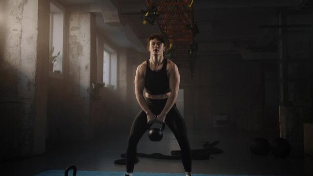 Slow motion of female weightlifter exercising, doing squats with kettlebells overhead