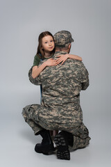 preteen kid hugging serviceman in military uniform during memorial day on grey.