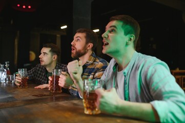 Sport, people, leisure, friendship, entertainment concept - happy male football fans or good yuong friends drinking beer, celebrating victory at bar or pub. Human positive emotions concept