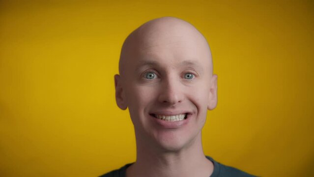 Man with blue eyes and bright skin looking straight towards the camera and makes an awkward smile on a yellow background, Real time.
