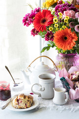 An arrangement of tea, scones and flowers against a bright sunny window.