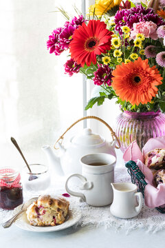 An arrangement of tea, scones and flowers against a bright sunny window.