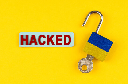 On the yellow surface is an open lock with a key and a sticker with the inscription - hacked - Powered by Adobe