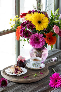 A beautiful flower arrangement with tea and scone in front, on a rustic board.
