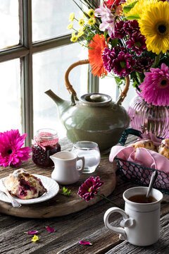 Tea and scones with a bright colourful flower bouquet on a rustic table.
