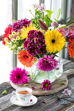 A bright colourful bouquet of flowers in a glass teapot shaped glass vase.