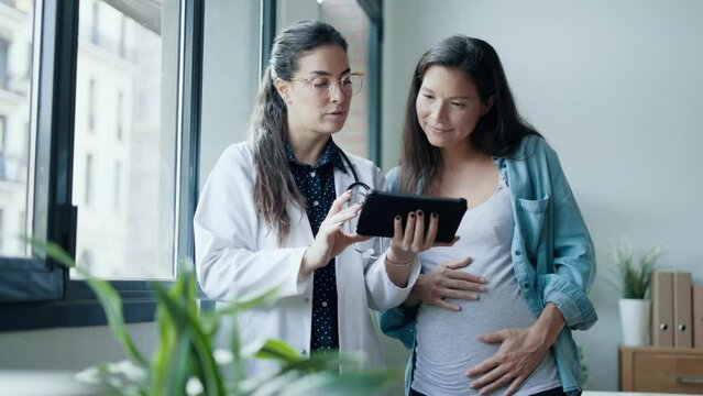 Video of female gynecologist doctor showing to pregnant woman ultrasound scan baby with digital tablet in medical consultation.