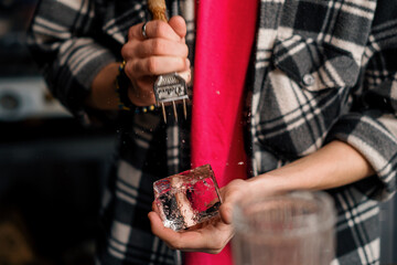 The bartender breaks the ice Close-up of male hands cracking ice with a sharp tool in a bar