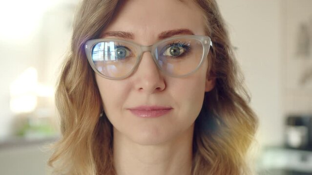 Close up of cute woman in spectacles with blond curly hair, light make-up. The woman looks directly into camera, blinks couple of times. High quality 4k footage
