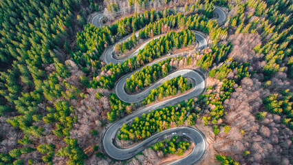 Aerial photography of a winding road in the mountains with serpentines and curves. Photography was shot from a drone at a higher altitude.