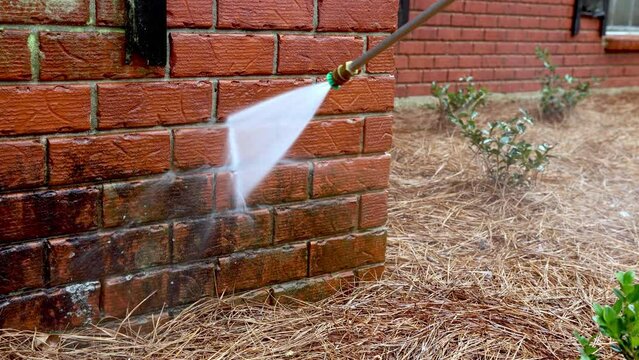 Pressure washer using water to clean a dirty brick wall on a house.