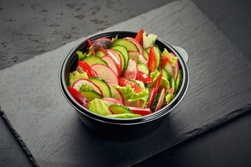 Salad of radishes, cucumbers, sweet peppers and lettuce in plastic bowl