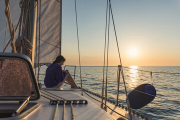 Woman enjoying a colorful sunset on a sailboat yacht sailing in the sea