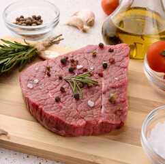 Raw piece of beef with spices pepper, rosemary sprig, salt and olive oil on a wooden board, top view