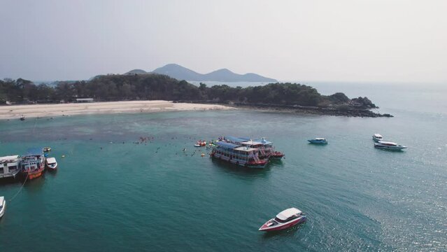 Small tropical island in middle of blue sea with tourists enjoying watersport leisure activities and boat sailing