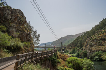 Obraz premium Wooden fence next to a hill with vegetation on the bank of the Mondego river and a bridge in the background