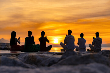 Silhouettes of group of young people meditating on the sunrise sun at the sea