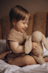 A baby sits on a couch with a stuffed animal.