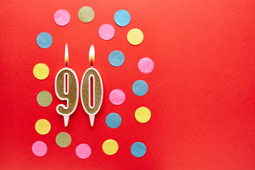 Number 90 on a red background with colored confetti. Happy birthday candles. The concept of...