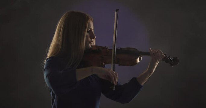 Beautiful blond woman playing violin against blue and violet smoke background.