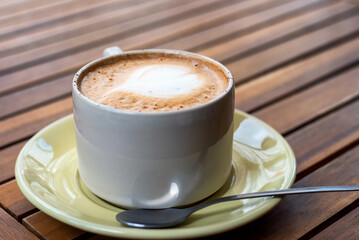 Coffee with foam art in white mug and light green saucer on wood table