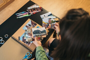 Image from above of an unrecognizable middle-aged woman selecting photos to be taped with washi...