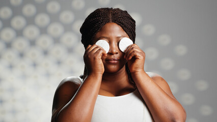 African american girl using cotton pads on camera, using toner and cleanser as beauty routine....