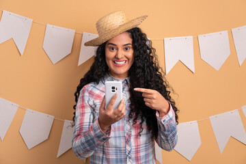 happy afro brazilian woman to Junina Party in Brazil in beige studio background. texting and typing...