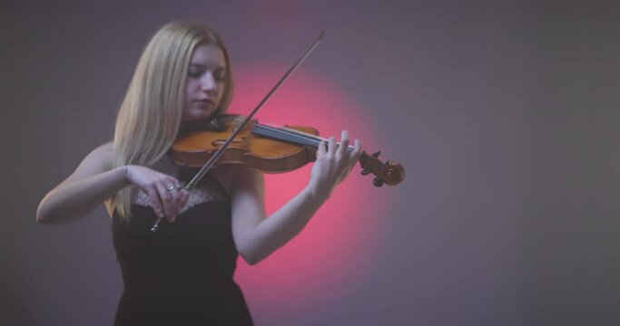 Beautiful blond woman playing violin against pink spotlight with smoke background.