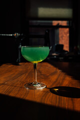 green absinthe drink in a coupe glass with on wooden table in the sun	