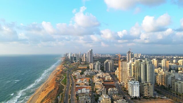 Netanya, Israel, September 3, 2022. Aerial view of the height of the city of Netanya at sunset. The sun illuminates the houses with golden rays. Blue sky with white clouds. High-quality 4k footage