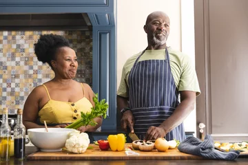 Plexiglas foto achterwand Happy senior african american couple wearing aprons and cooking in kitchen © WavebreakMediaMicro