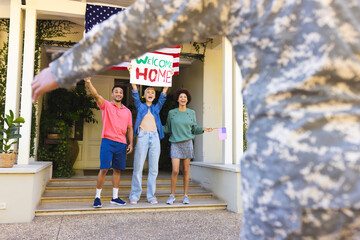 Happy diverse group of friends greeting biracial male american soldier outside the house
